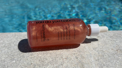 Bottle of 'you do your babes' body oil berry naughty product on a concrete surface with a pool in the background