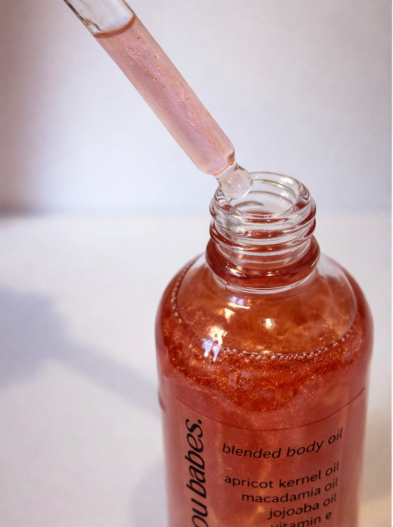 Bottle of pink shimmer blended body oil with a dropper on a white background