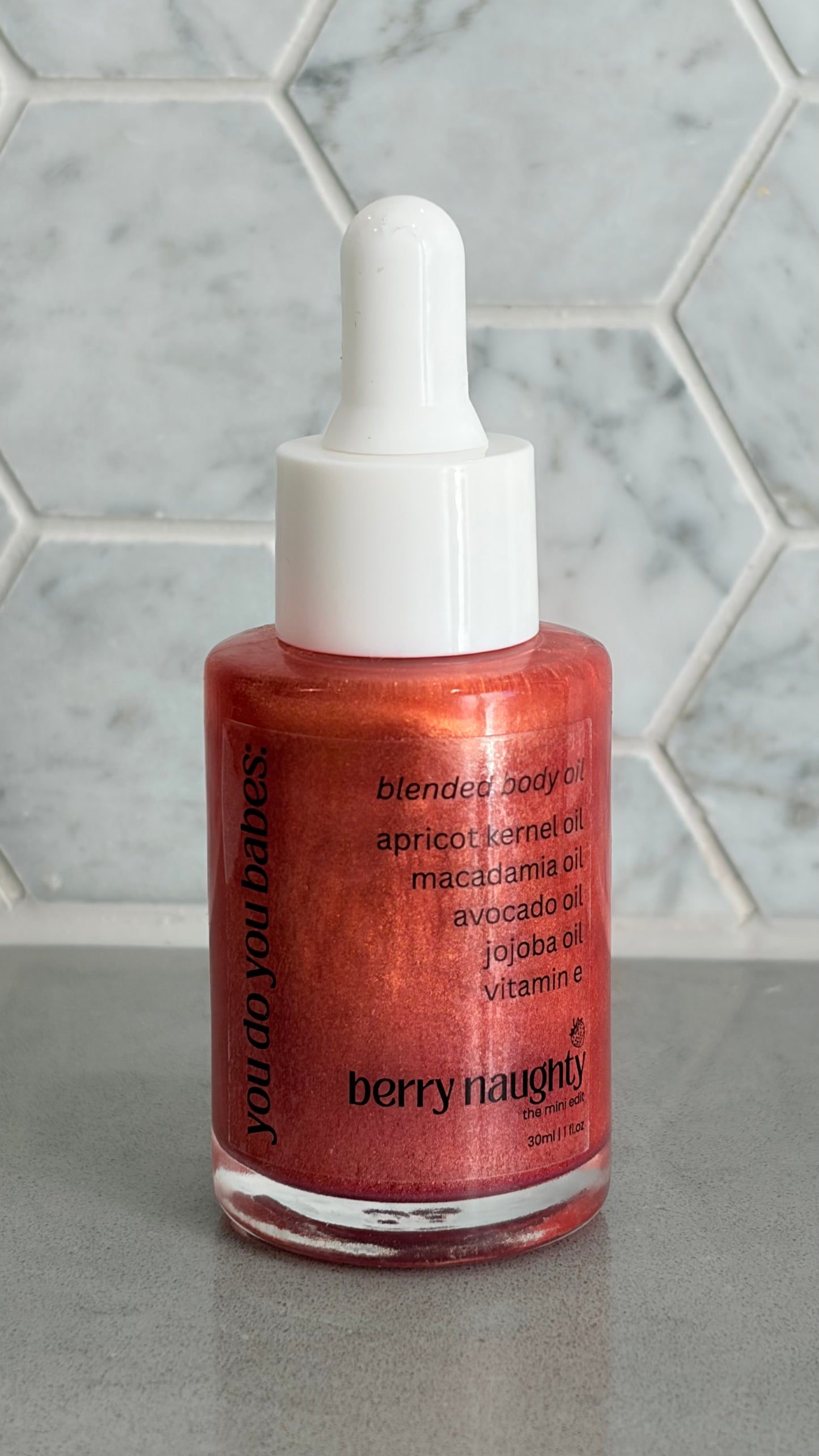Bottle of berry naughty body oil on a grey surface with a marble background