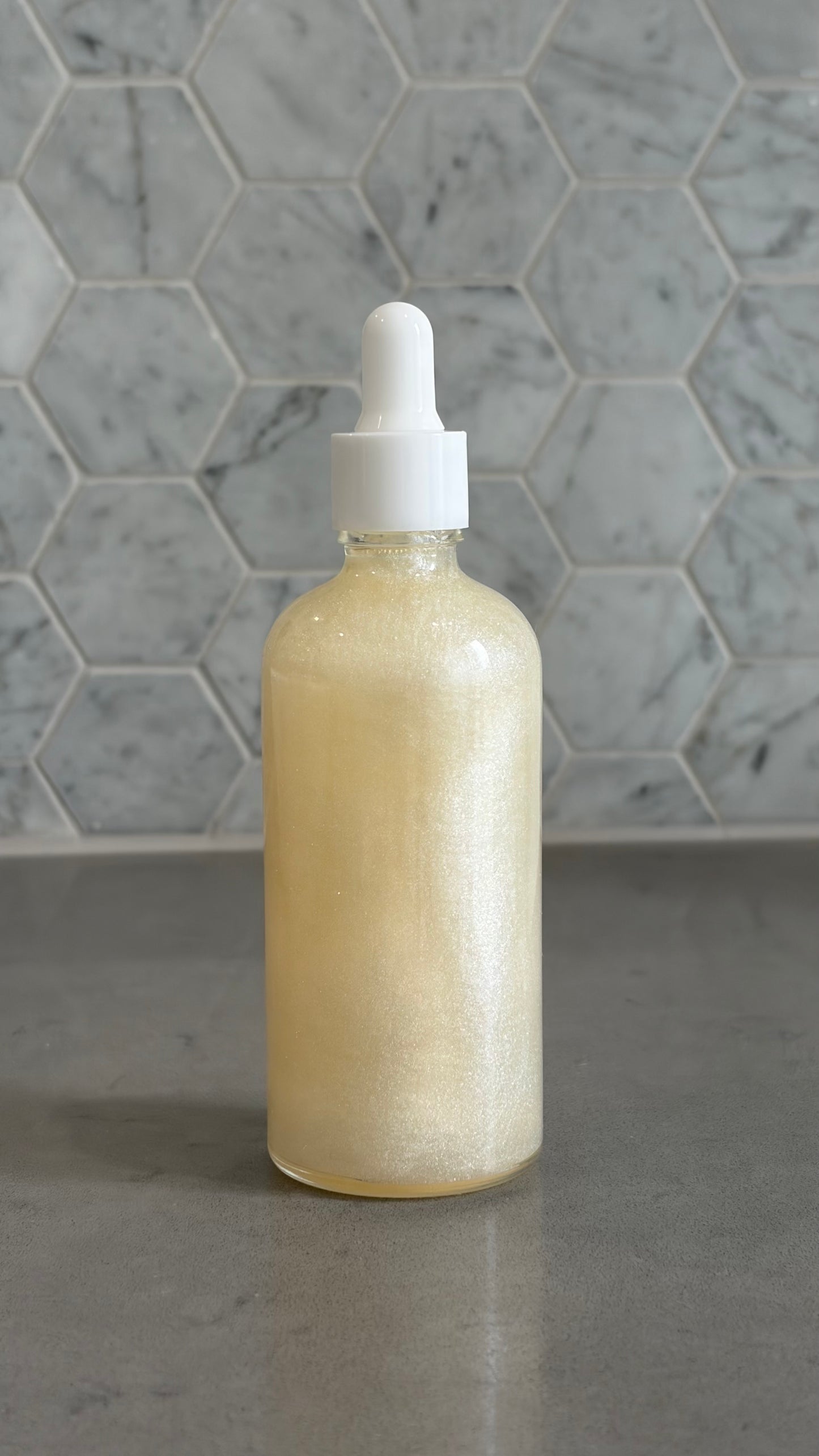 Bottle of 'you do you babes' coco glow blended body oil against a grey tiled wall.