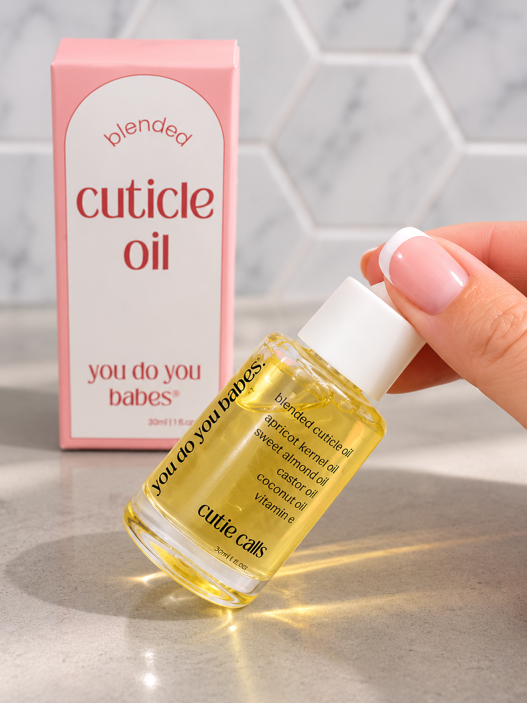 Bottle of cuticle oil with a pink box labeled 'blended cuticle oil you do you babes' on a neutral background.