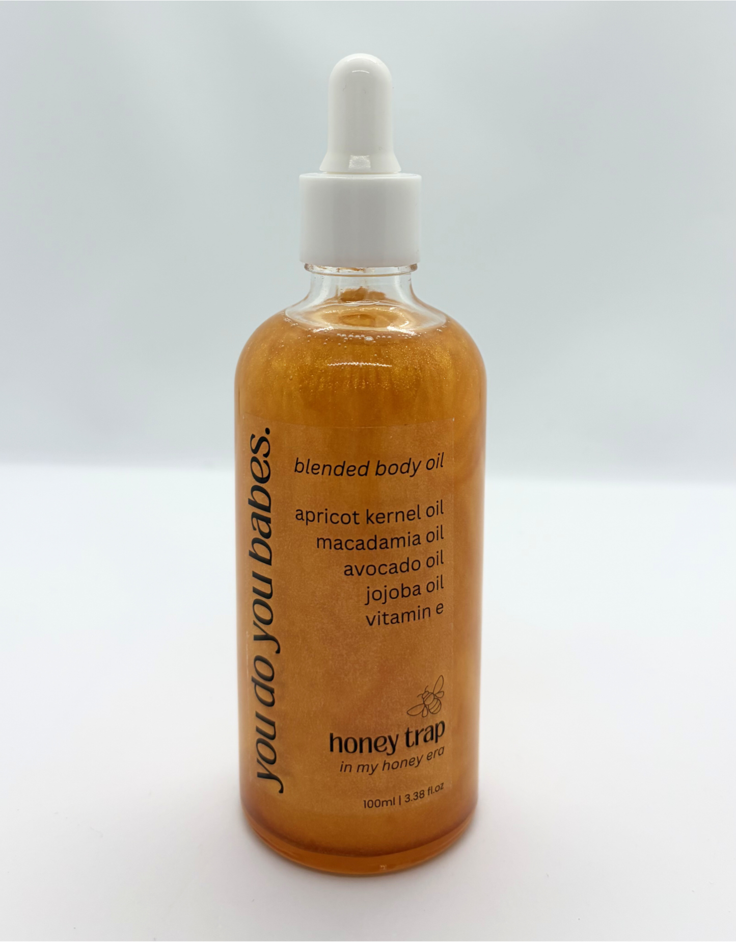 Bottle of HONEY TRAP blended body oil with a dropper on a white background