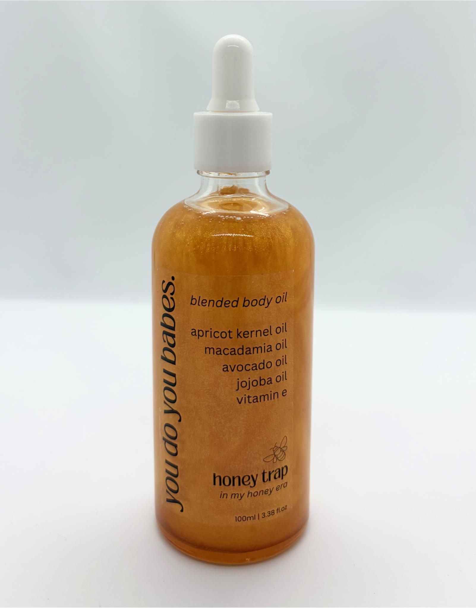 Bottle of HONEY TRAP blended body oil with a dropper on a white background