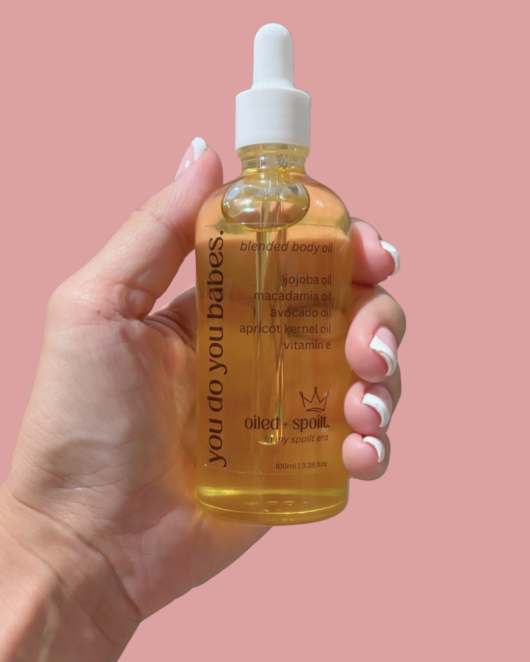Hand holding a bottle of 'you do you babies' blended Oiled and Spoilt body oil against a pink background