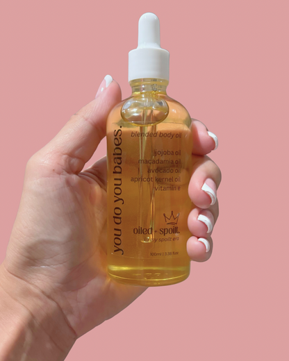 Hand holding a bottle of 'you do you babies' blended Oiled and Spoilt body oil against a pink background