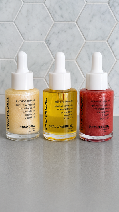 Three bottles of you do you babes skincare oils on a grey surface with a tiled wall background.