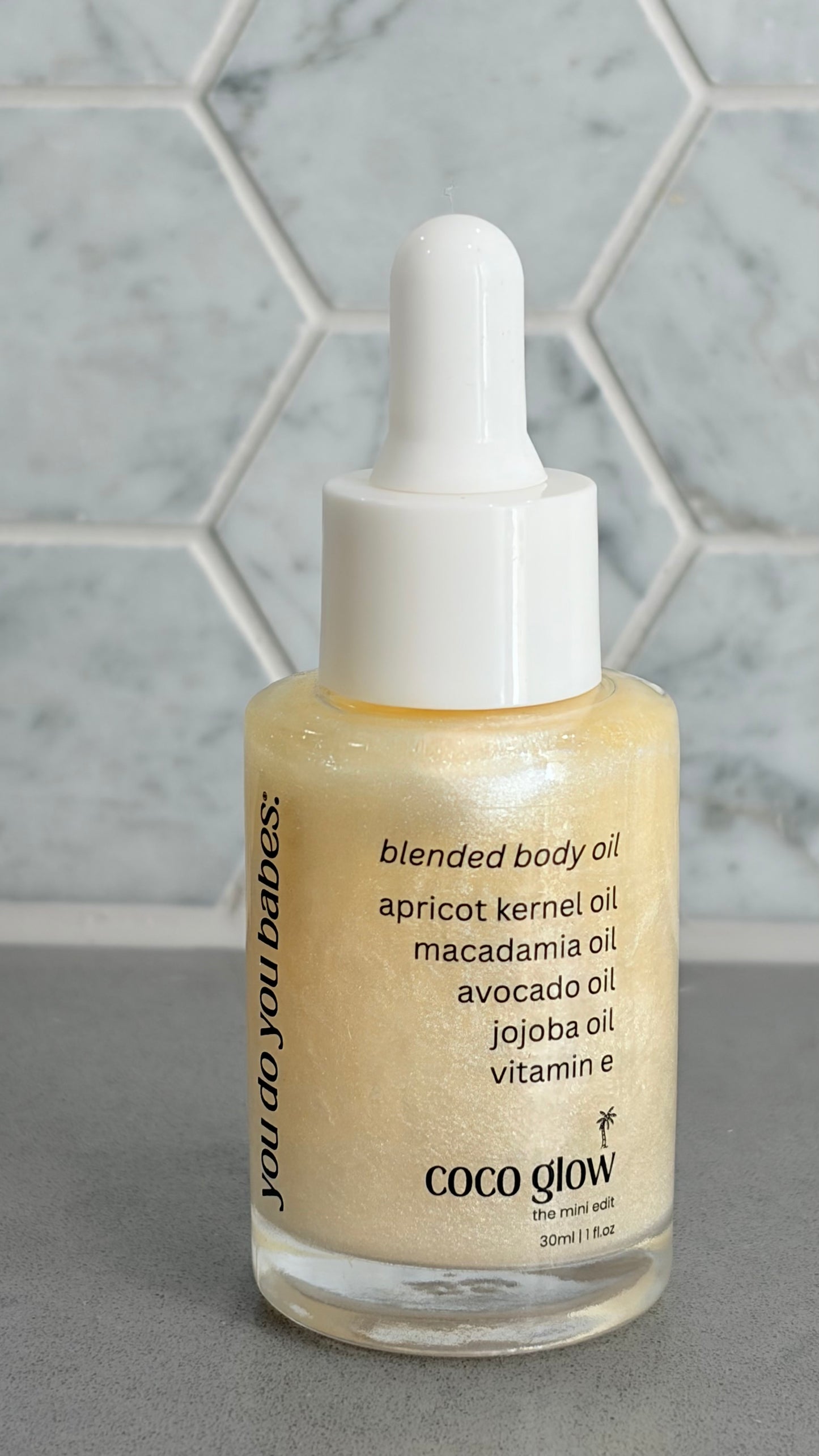 Bottle of Coco Glow blended body oil with a dropper on a grey surface.