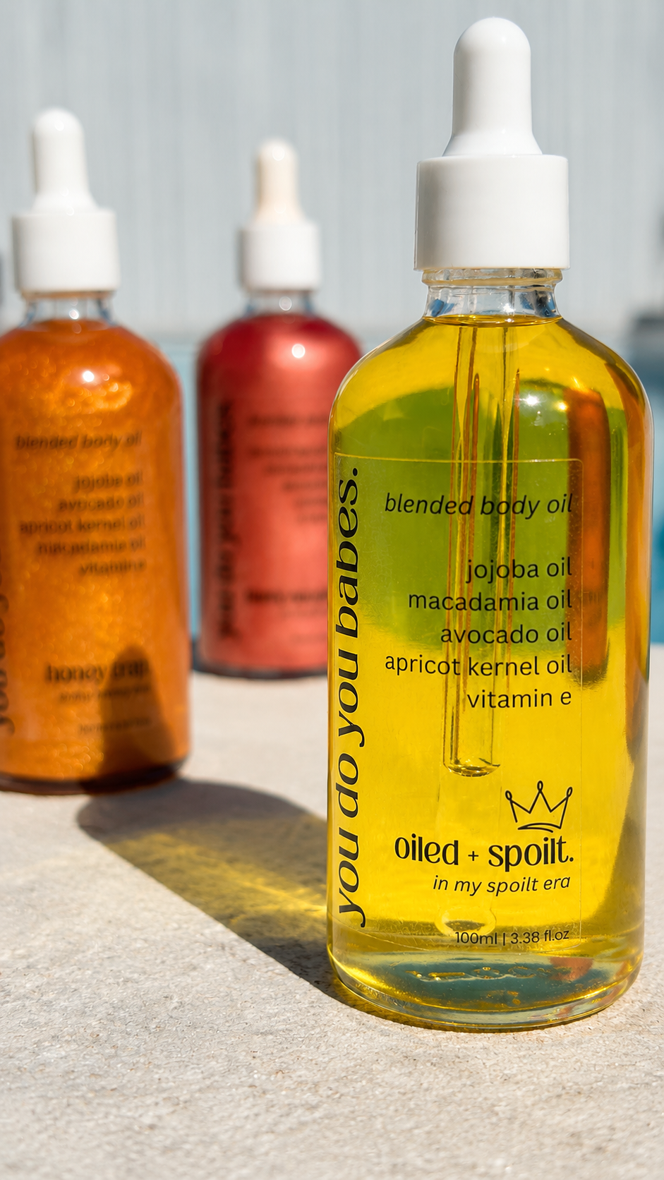 A glass dropper bottle of blended body oil in the foreground, with two blurred bottles in the background.