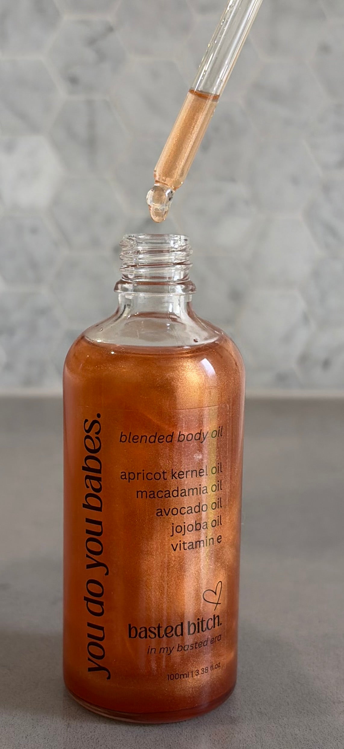 Bottle of blended basted bitch body oil with dropper on a gray background