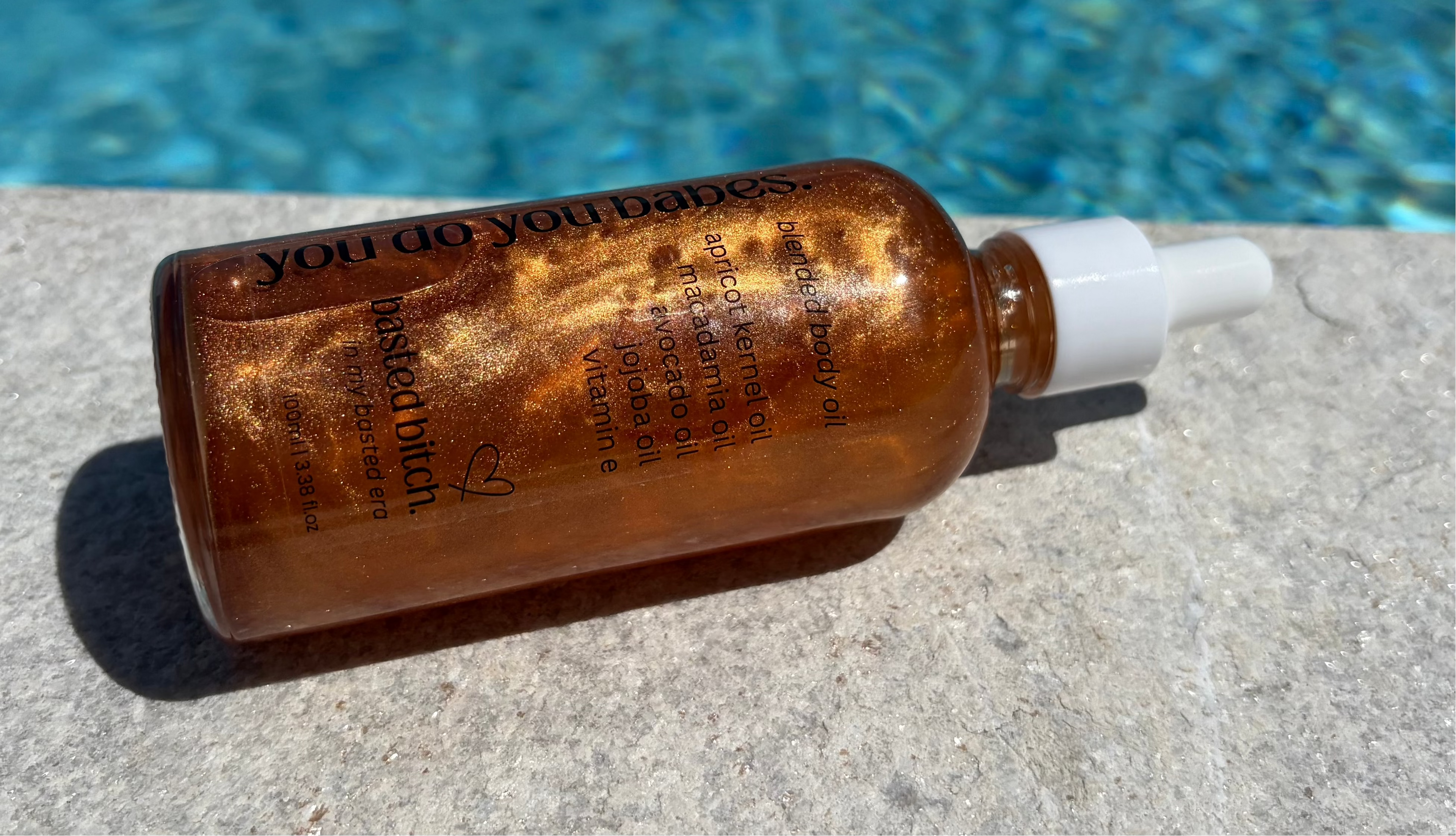 Bronzed shimmer bottle of body oil from you do you babes near a pool