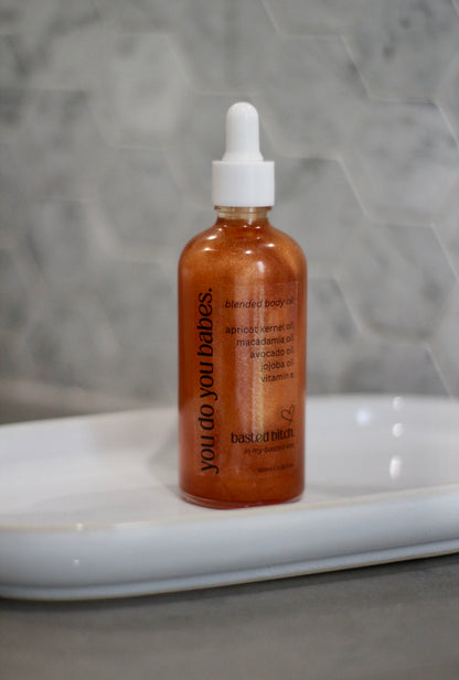 Bottle of 'you do you babies' skincare body oil on a white surface with a gray textured background