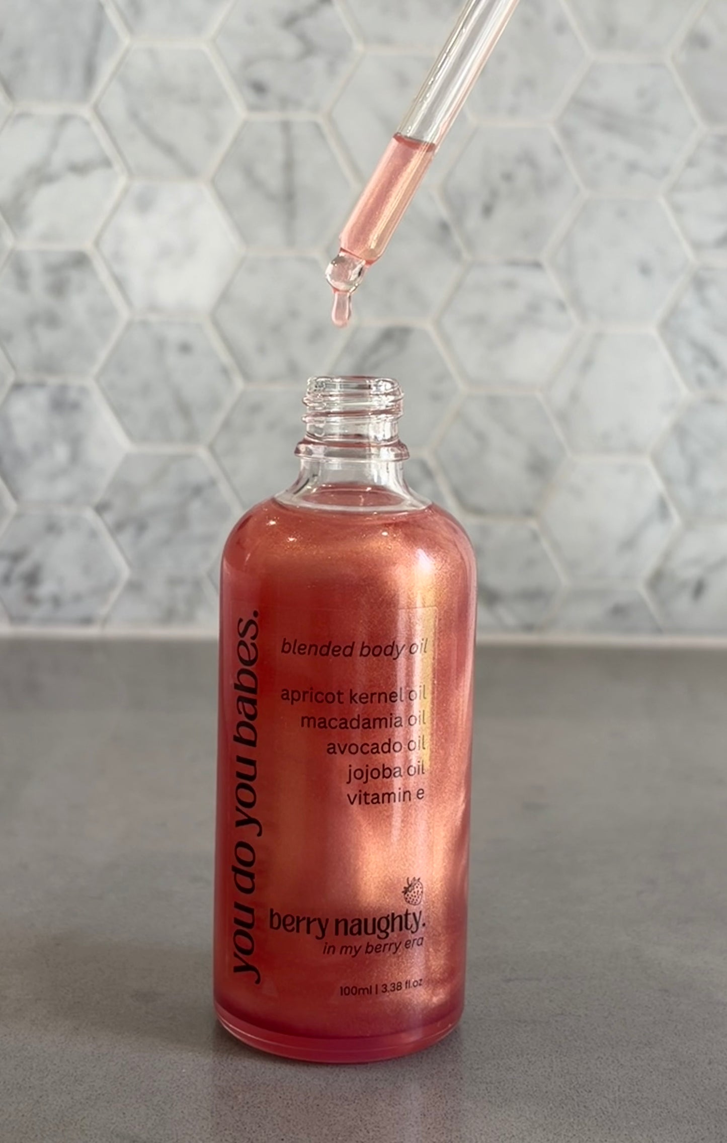 Bottle of blended body oil with a dropper on a gray surface and marble background