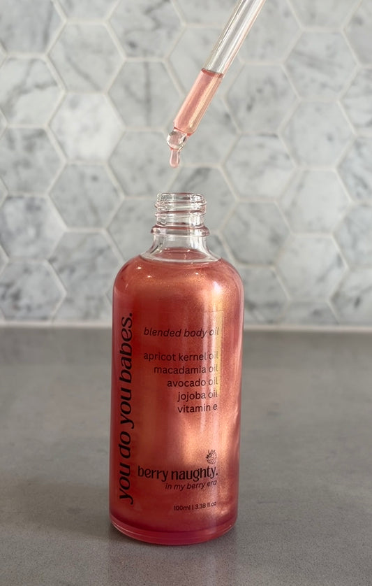 Bottle of blended body oil with a dropper on a gray surface and marble background