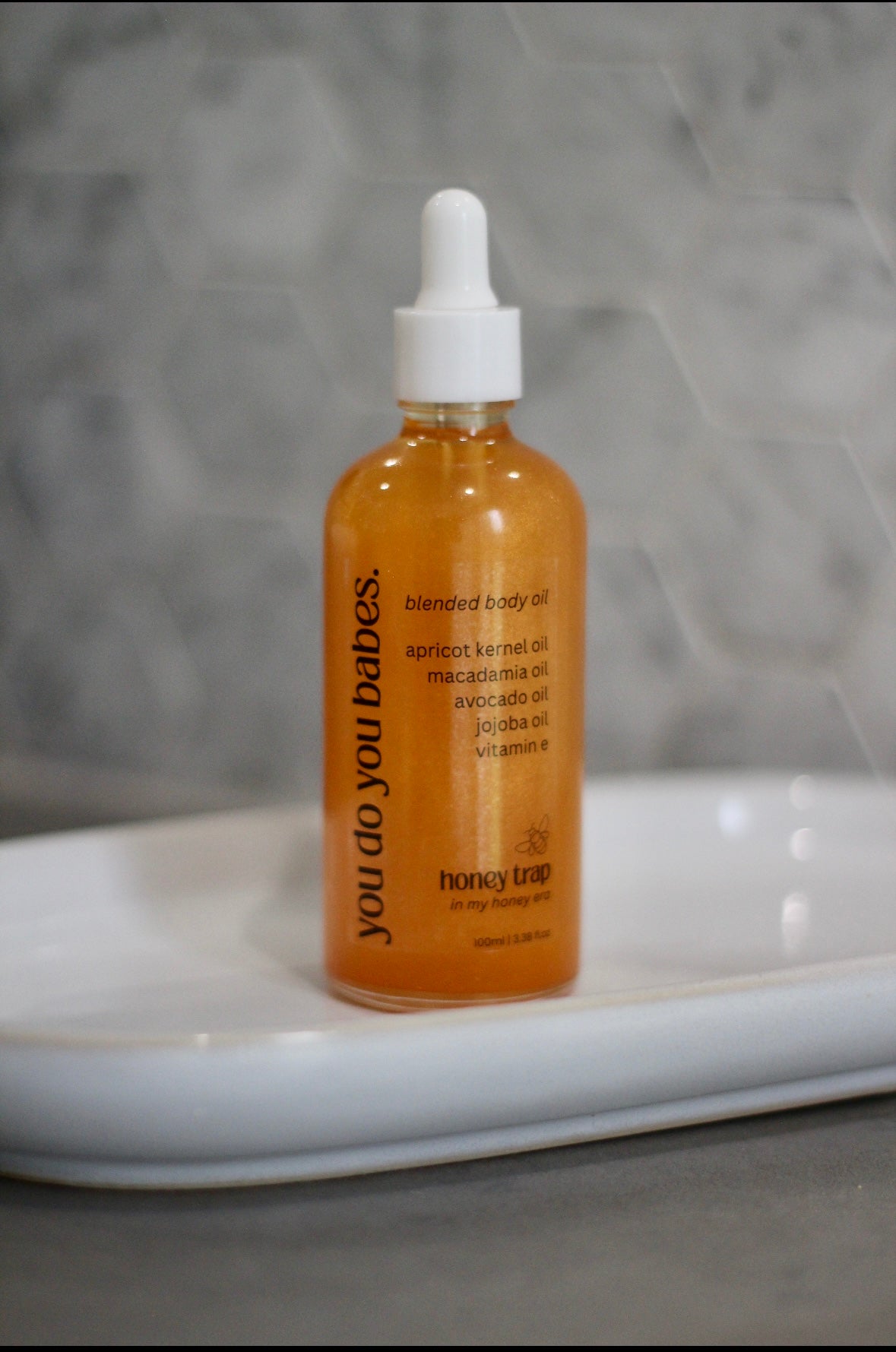 Bottle of 'you do you babes' honey trap oil on a grey background