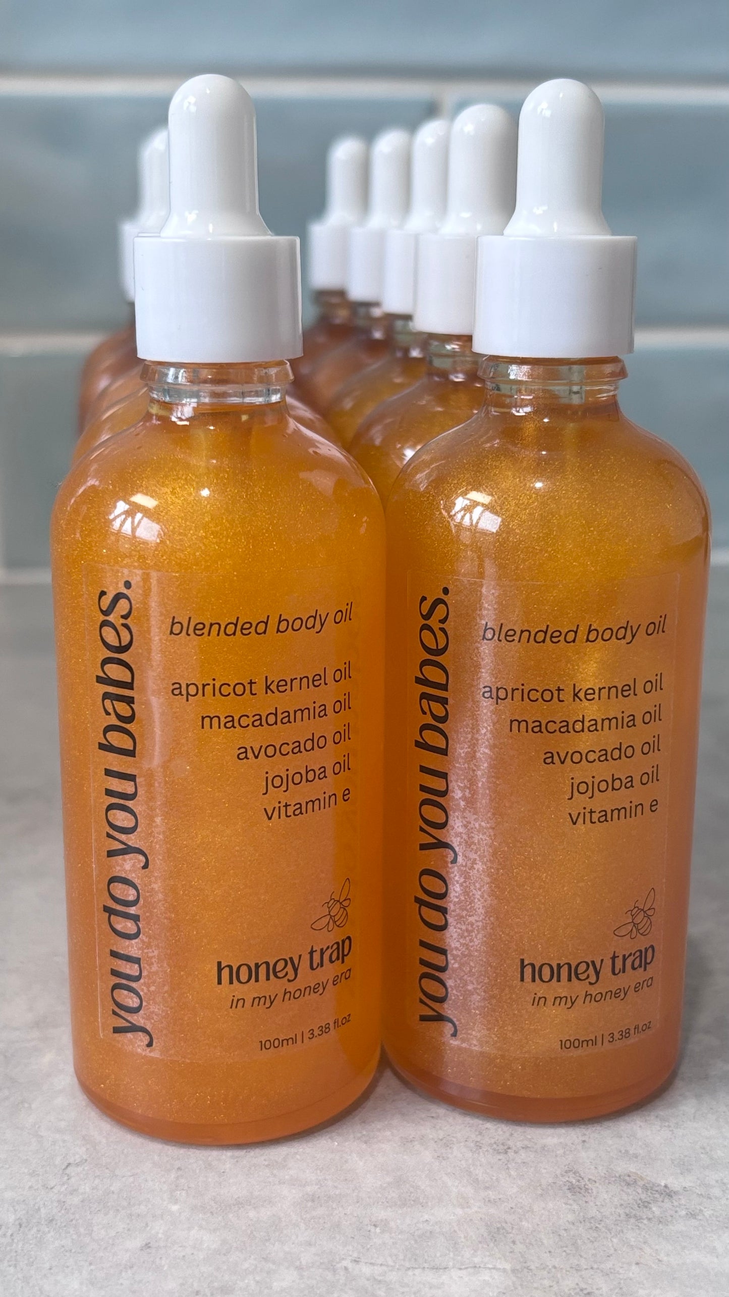 Multiple bottles of 'you do you babes' blended body oil on a gray surface.