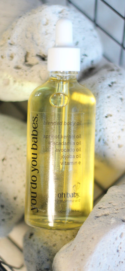 Bottle of Oh baby body oil with a white cap on a stone surface