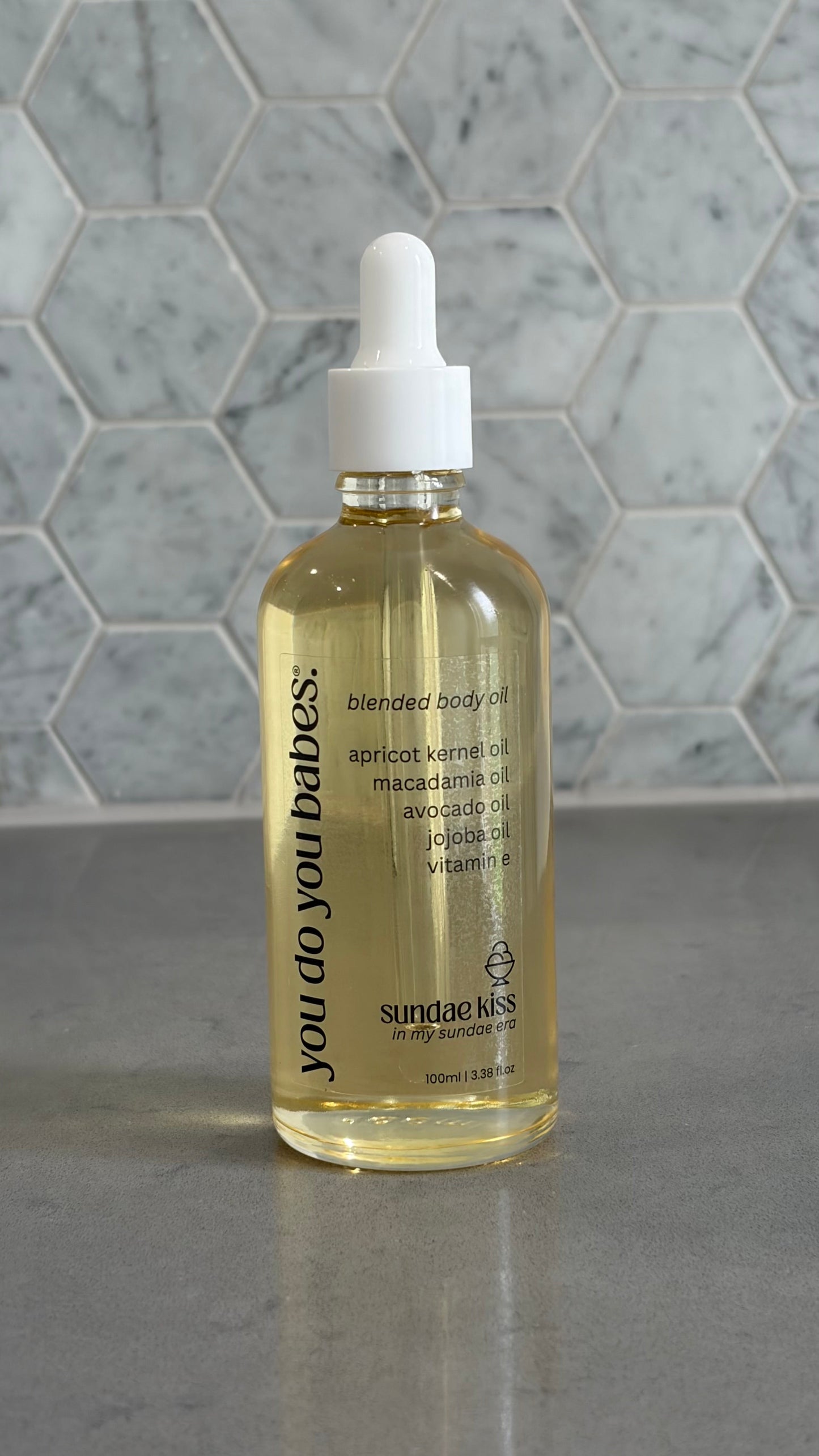 Bottle of 'you do you babies' sundae kiss body oil on grey surface with a marble background