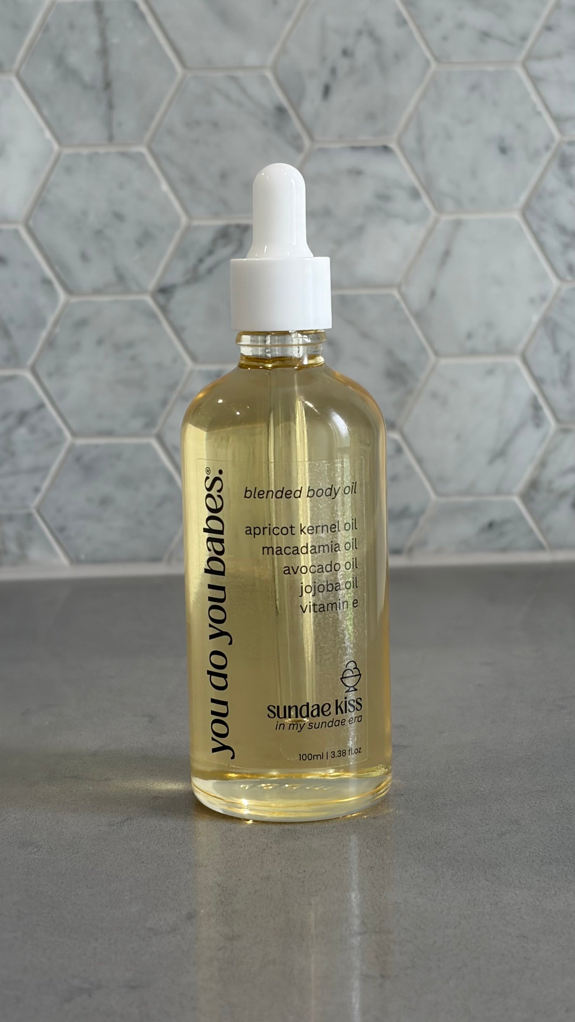 Bottle of 'you do you babies' sundae kiss body oil on grey surface with a marble background