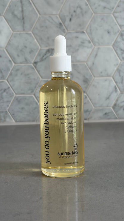 Bottle of 'you do you babies' sundae kiss body oil on grey surface with a marble background