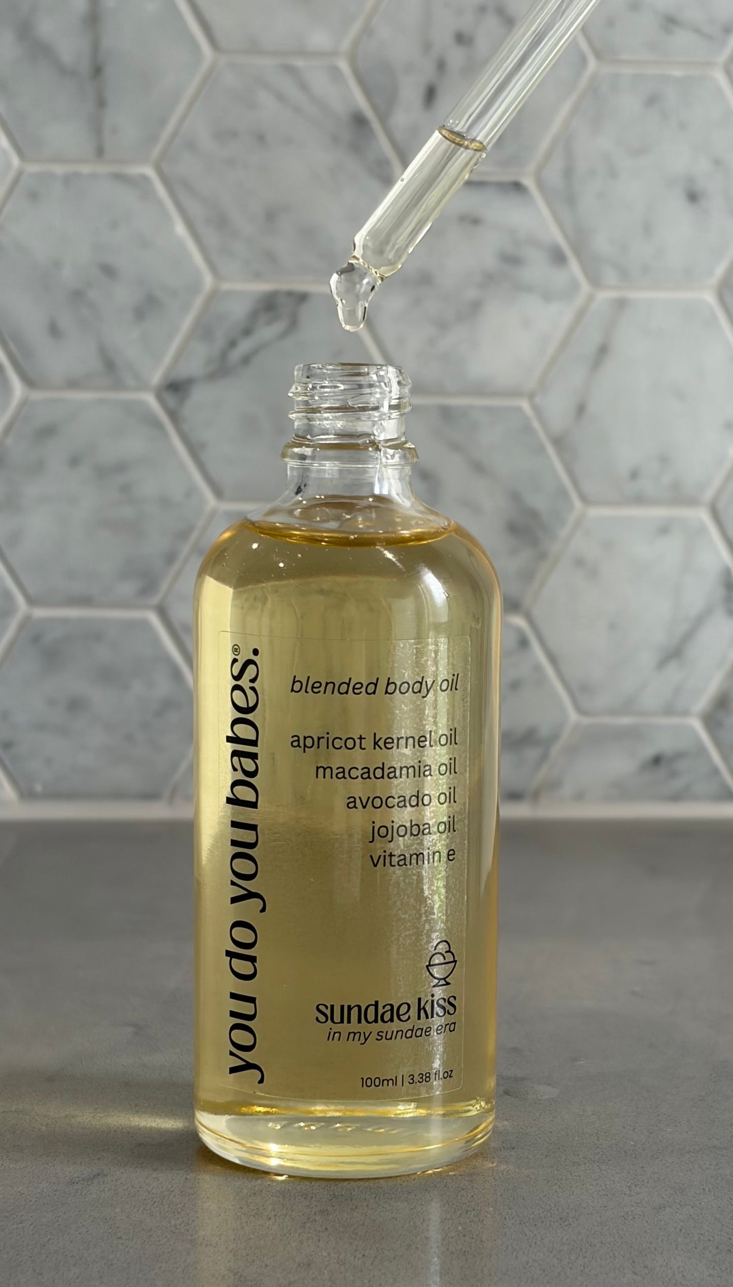 Bottle of 'you do you babes sundae kiss' blended body oil with a dropper on a grey surface.