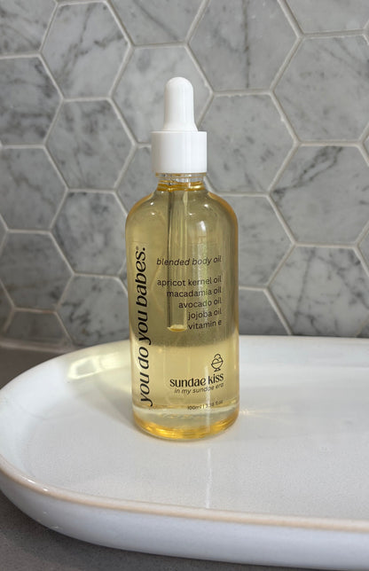 Bottle of sundae kiss body oil with a dropper on a white surface against a marble background