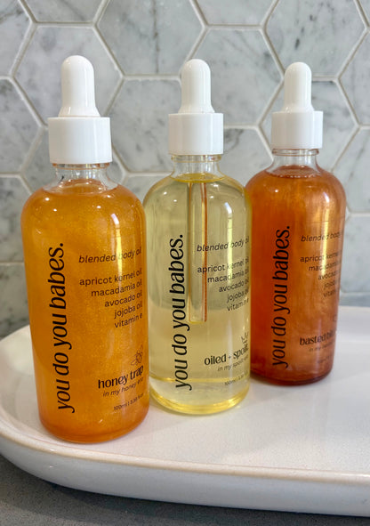 Three bottles of 'you do you babes' body oils on a white tray with a tiled wall background.