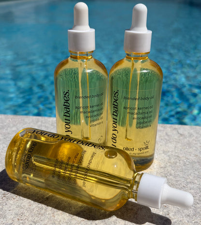 Three bottles of 'you do you babes' blended body oil by a poolside.
